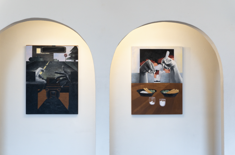  Two paintings by artist April Werle are displayed in arched wall niches. The left artwork depicts a nighttime car interior with silhouetted hands on the steering wheel, illuminated by an urban road scene. The right artwork features two hands preparing or eating noodles over a table with bowls of food and drinks, set against a vibrant background. The exhibition, titled Secret Life of a Multicultural Couple, uses muted and bold tones to convey intimate moments in everyday life.